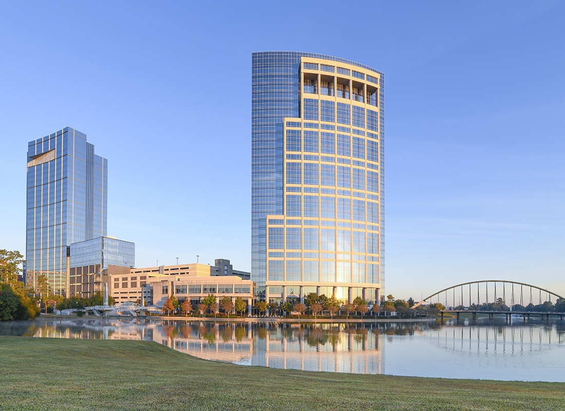 The Woodlands, TX - Distant View of The Woodlands, TX Displaying Tall Buildings With Gold-Like Exterior Frames and a Body of Water With a Bridge